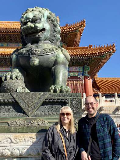 Julijana and Zarino stand in front of a large bronze statue of a lion