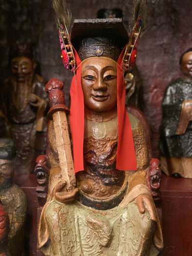 A small wooden statue of a wise man at Man Mo Temple, wearing a black cap and red ribbons