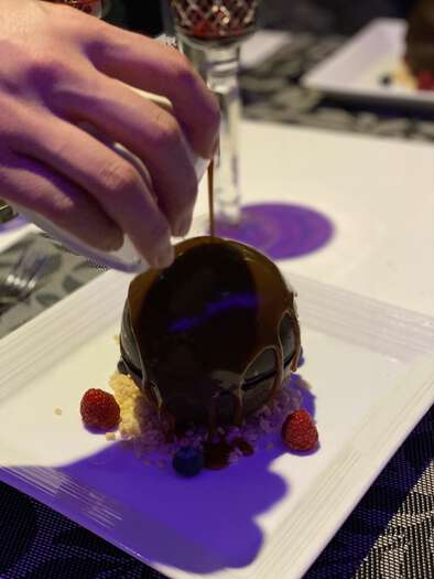 Chocolate sphere dessert being melted with warm sauce, 1 of 3