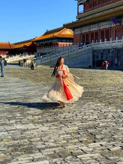 Girl in traditional Chinese dress, spinning for the camera at the Forbidden City